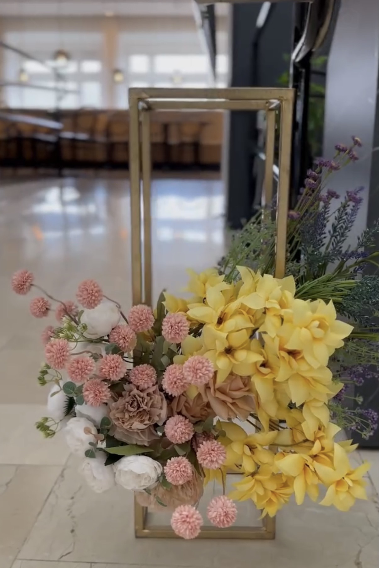 Blomsterarrangemang i guldstativ med gula och rosa toner