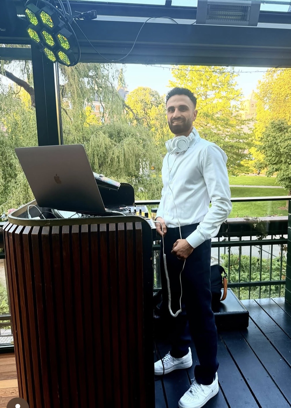 Leende DJ med hörlurar vid DJ-bås på en glasad veranda i dagsljus